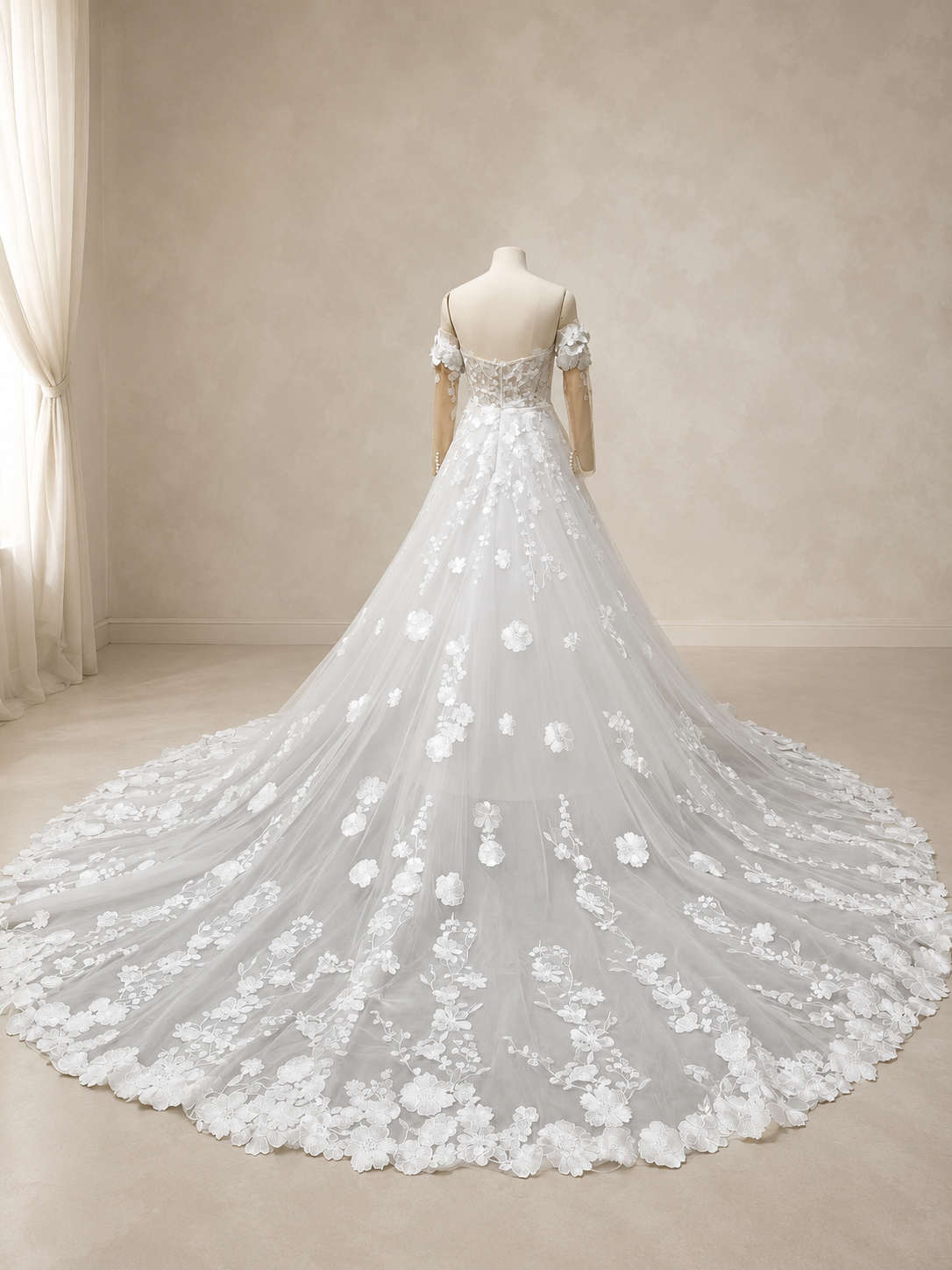 Wide rear view of an ivory tulle A-line bridal gown displaying the flowing back skirt and chapel train with embroidered floral lace motifs and a botanical lace border.