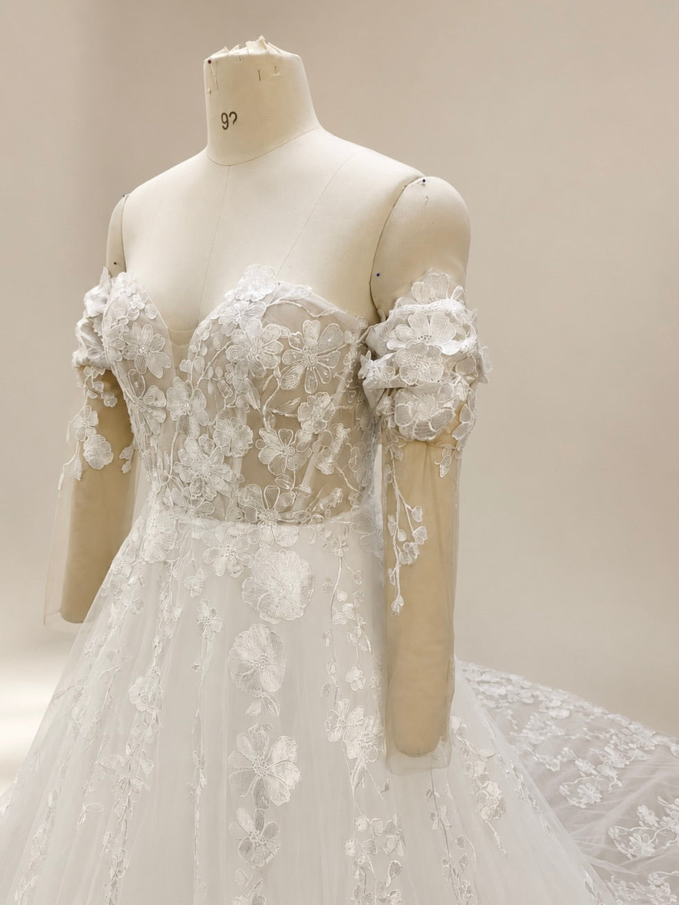 Close-up side view of a sweetheart bridal bodice with floral lace appliqué and a detachable off-the-shoulder illusion sleeve decorated with dimensional embroidered flowers.