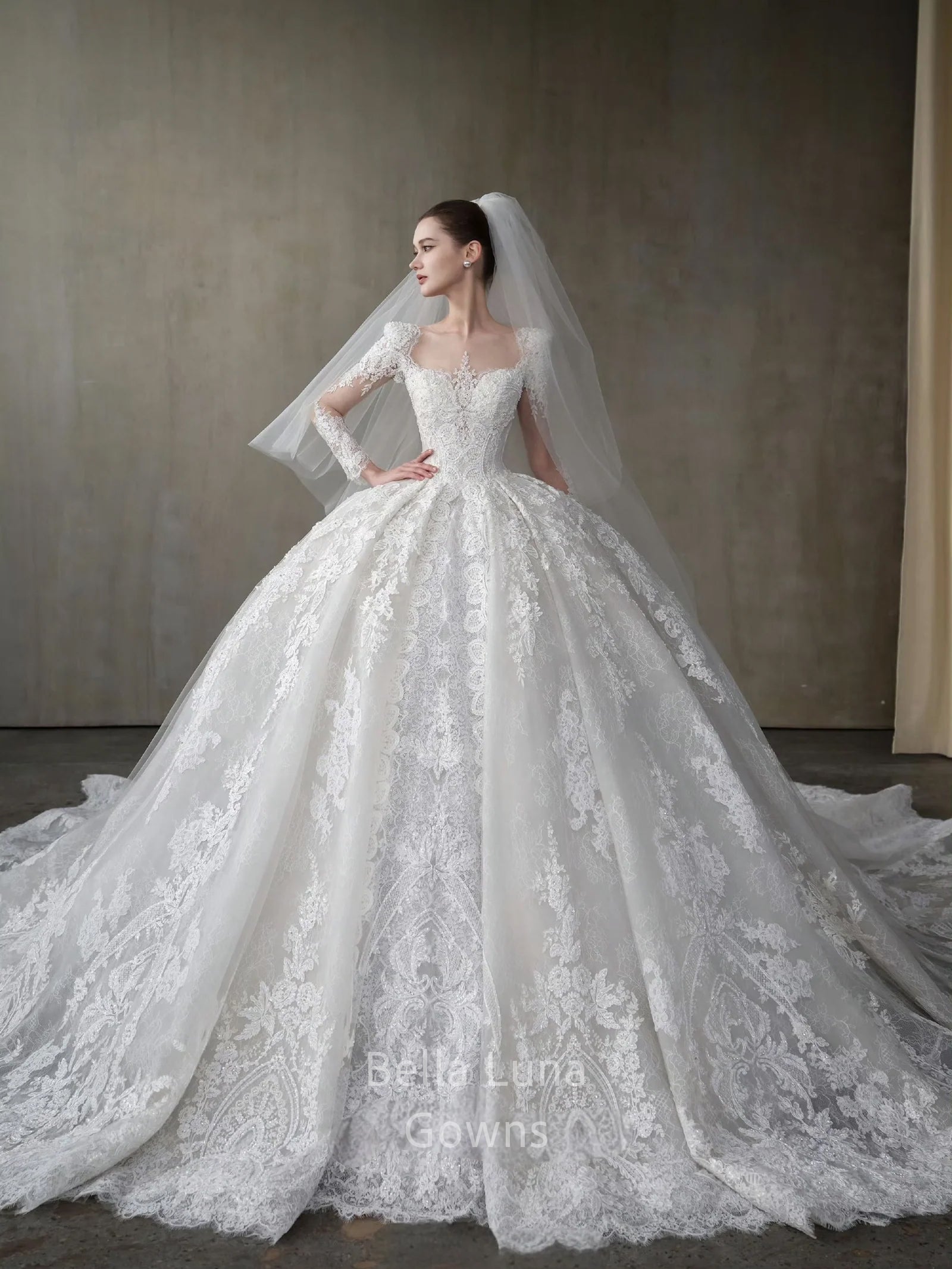 Front view of Genevieve off-white lace bridal ball gown with square neckline, long sleeves, full skirt, and veil styling