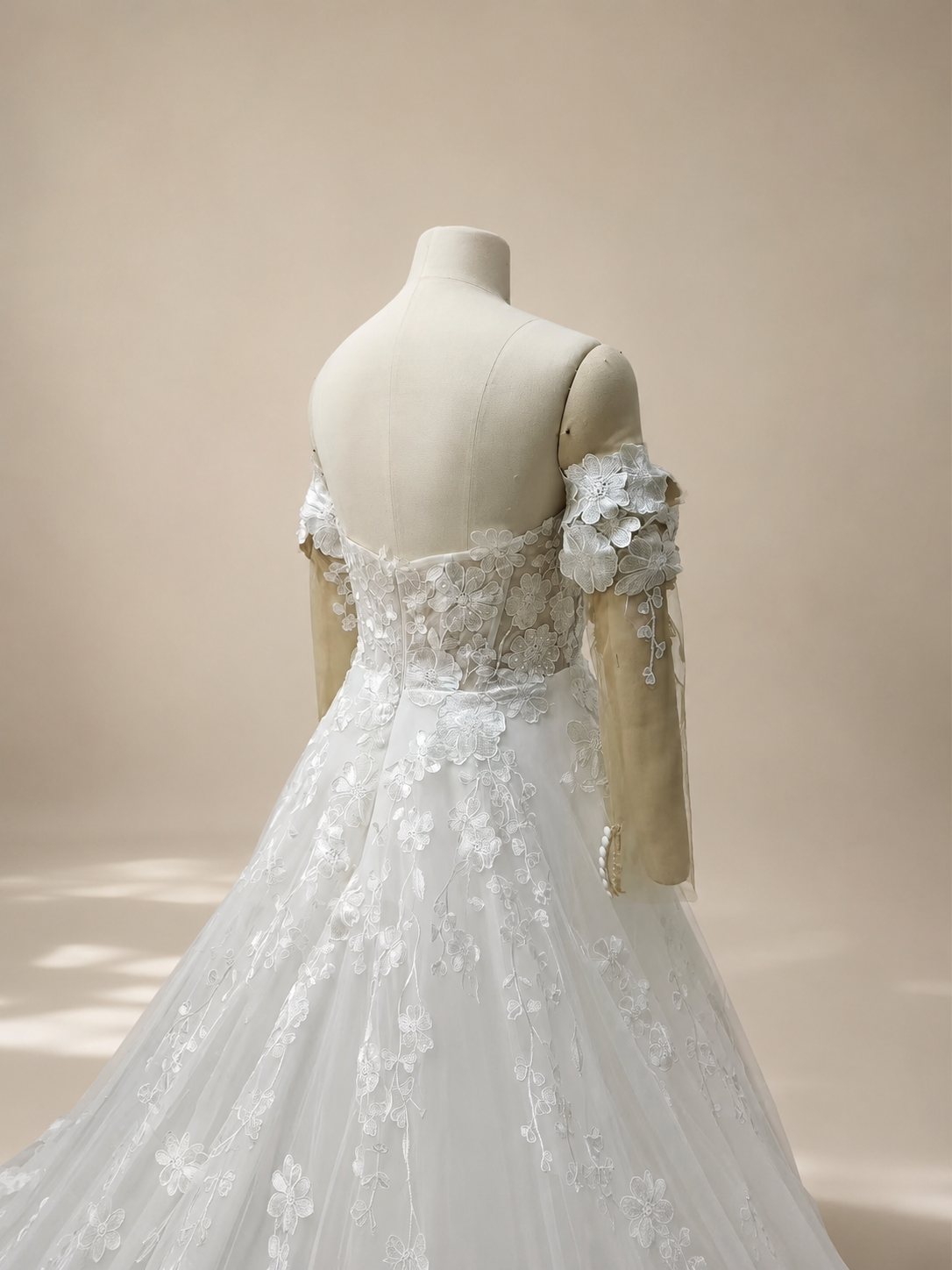 Close-up back view of an ivory lace wedding dress with a center-back zipper, floral embroidered bodice, detachable illusion sleeves, and fabric-covered sleeve cuff buttons.