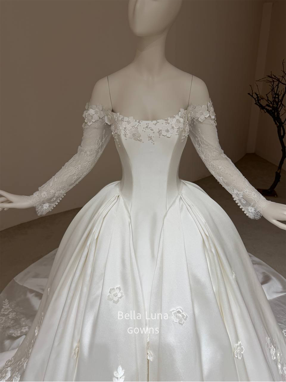 Front view of the Aveline off-white satin basque-waist ball gown with long lace sleeves and floral-and-leaf appliqués