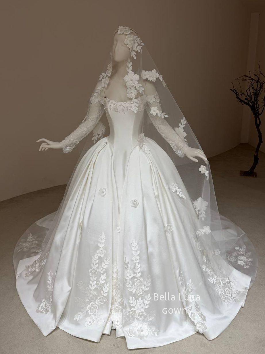 Front view of the Aveline off-white satin basque-waist ball gown with long lace sleeves and floral-and-leaf appliqués