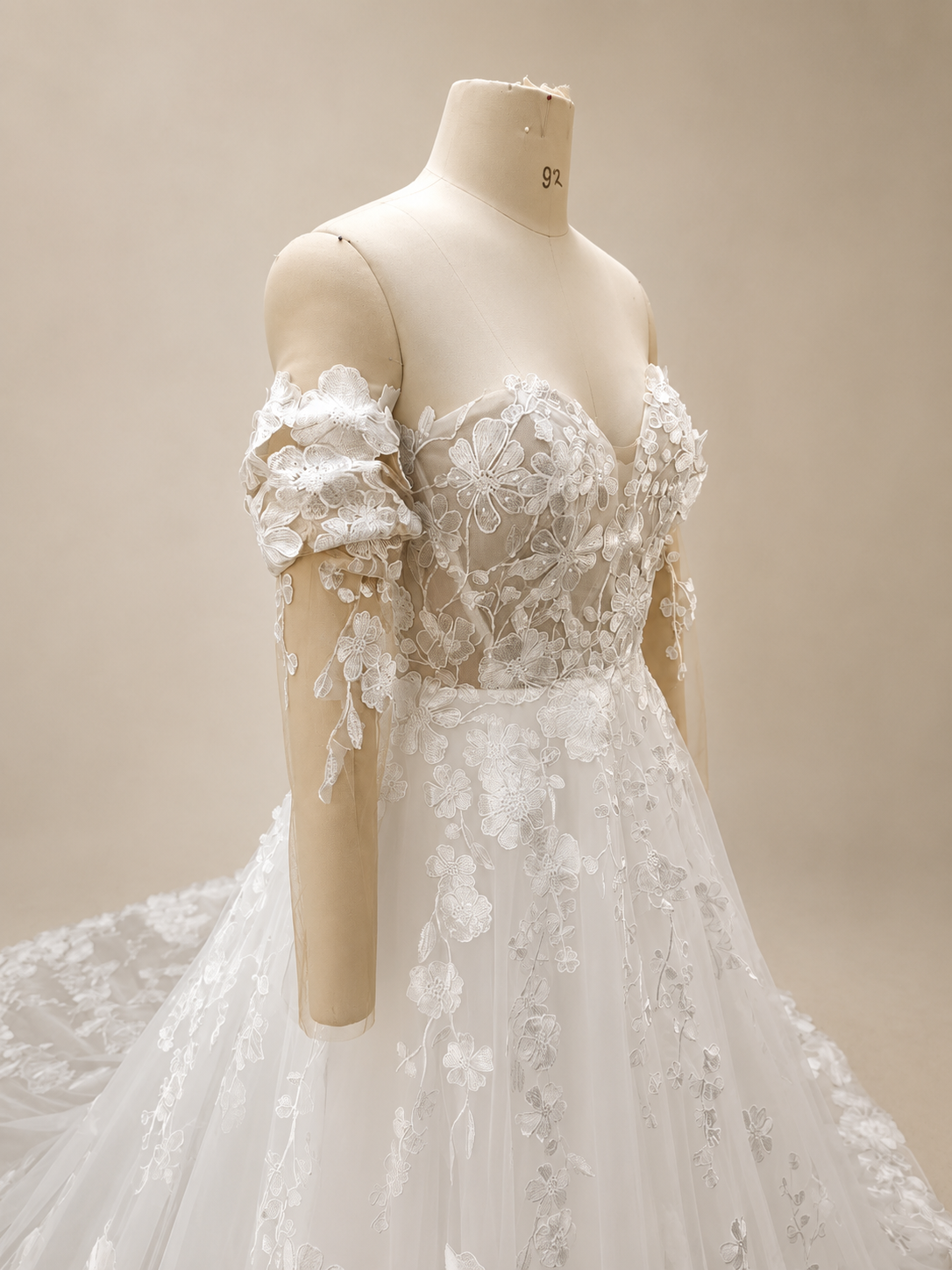 Close-up side view of a sweetheart bridal bodice with floral lace appliqué and a detachable off-the-shoulder illusion sleeve decorated with dimensional embroidered flowers.