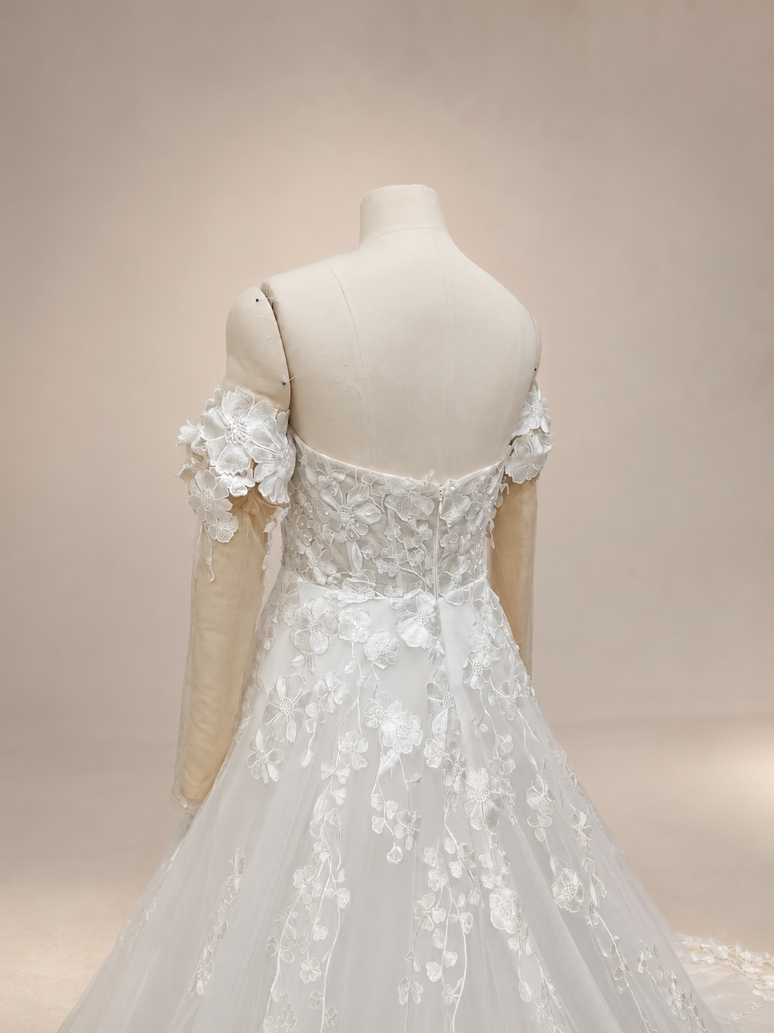 Close-up back view of an ivory lace wedding dress with a center-back zipper, floral embroidered bodice, detachable illusion sleeves, and fabric-covered sleeve cuff buttons.