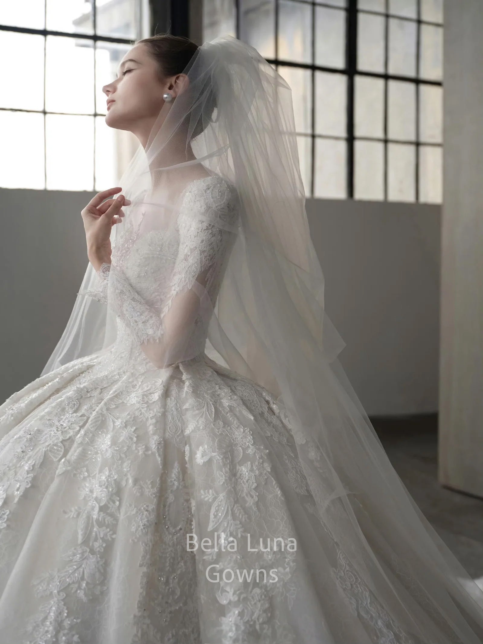 Side close-up of Genevieve off-white lace bridal ball gown with long lace sleeves, veil styling, and full skirt