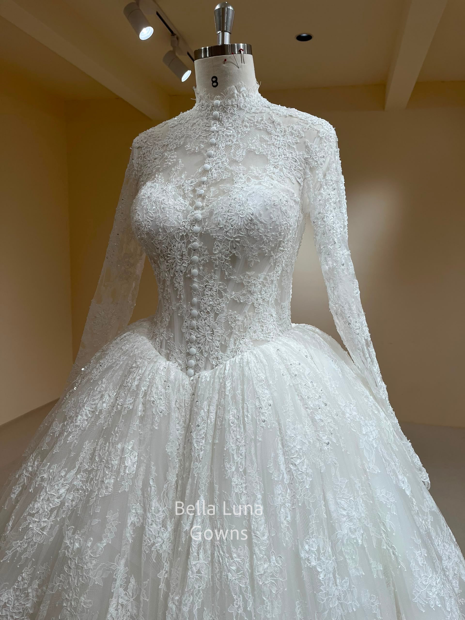 Front three-quarter view of the Theodora high-neck French lace ball gown with long sleeves and basque waist